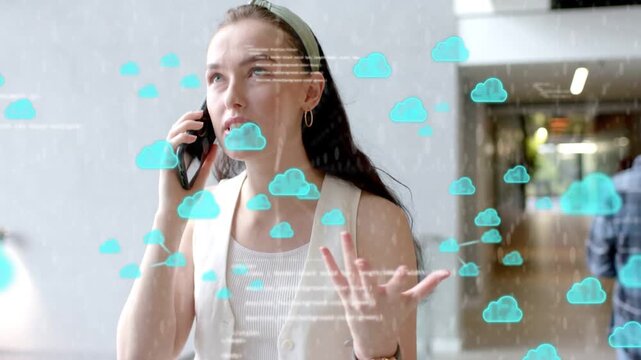 Woman speaking on phone in hall, initiating teal cloud icons hovering around showing business data
