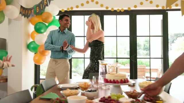 Couple entering sliding doors reacting while guests revealing balloons banner and cake for events