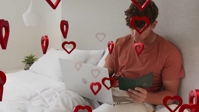 Student reading green booklet and using laptop as red hearts rising and covering laptop, education