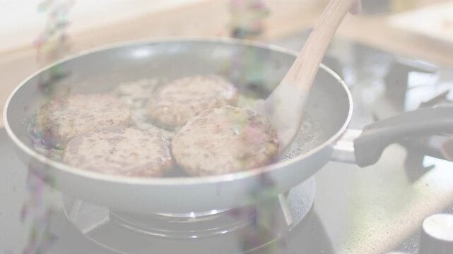 Culinary home cook hand nudging spatula from right, turning burger patties to brown evenly