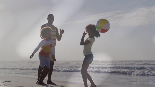 Father watching as children catching and passing beach ball being tossed, backlit bonding marketing