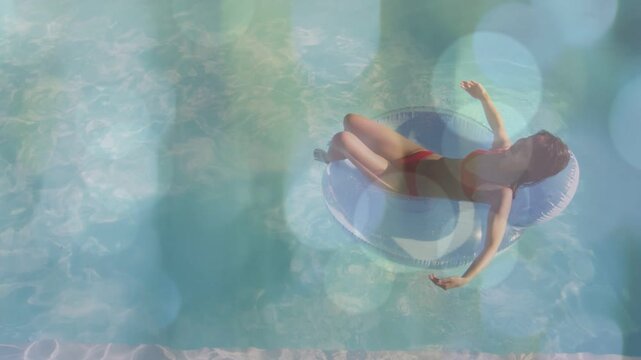Woman lying on blue ring in pool for leisure, sun causing head turning, stretching bokeh circling