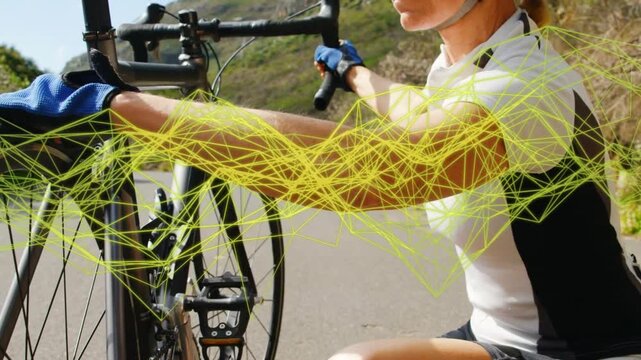 Female cyclist kneeling, checking front wheel before ride on coast road, yellow mesh crossing face