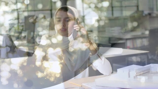Designer receiving call, checking laptop and model for feedback, bokeh overlay moving over subject