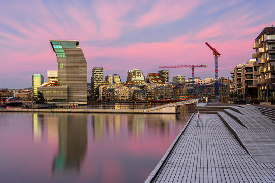 View of the Munch Museum and Barcode Project skyline reflected in the water under a pink sunset sky from the waterfront boardwalk in Oslo, Oslo, Norway.