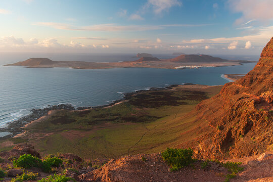 View of the volcanic landscape overlooking the island of La Graciosa with reddish cliffs and blue ocean at sunset in Lanzarote, Canarias, Spain.