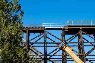 Naklejka premium Old wooden train trestle bridge on a sunny blue sky day, temporary wood safety fence, structural repairs construction project 