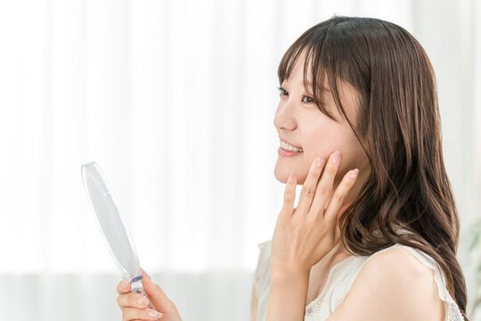Asian woman in the mirror doing skincare (beauty, cosmetics, skin, anti-aging)