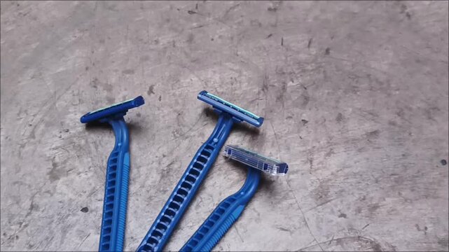 Top view of old used blue plastic disposable razors scattered on a grey concrete surface