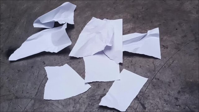 Top view of ripped white paper fragments and shredded waste sheets scattered on a gray concrete industrial background.