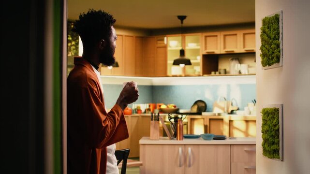 African american man, drinking coffee, relaxing at home, mug in his hands, enjoying natural peace and cozy moment with soft light for a reflective ambience. Person on the weekend, tea time.
