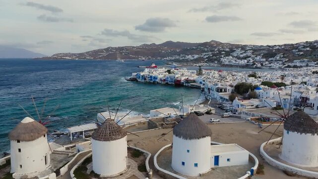 Aerial pullback shot revealing windmills of Mykonos on Greek Island with blue ocean in background, Cyclades island