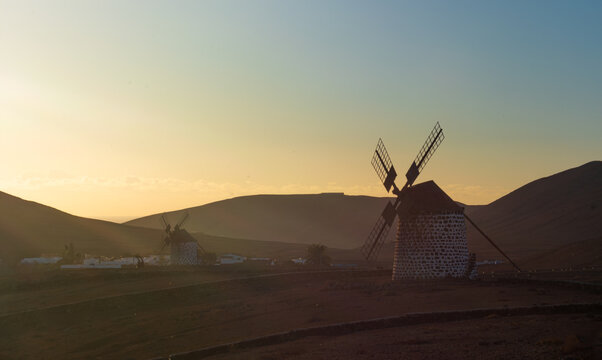 View of traditional stone windmills silhouetted against the golden sunset light and volcanic hills in Lanzarote, Canarias, Spain.