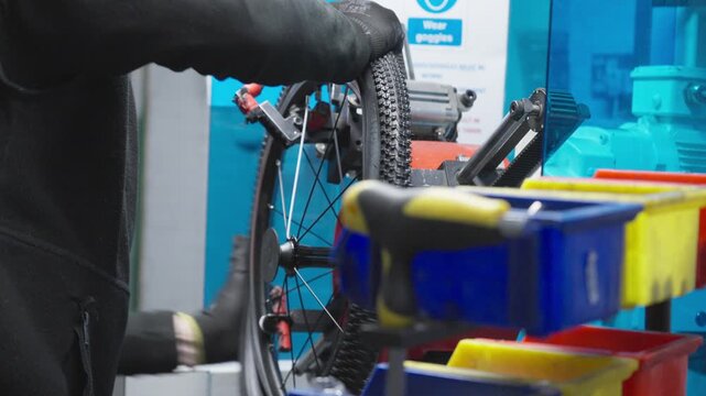 Close up of factory technician hands fitting a treaded tyre onto a bike rim.
