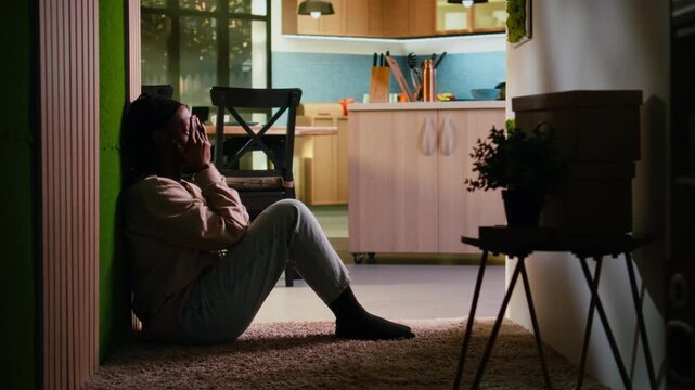Lonely depressed woman overwhelmed by problems and disappointment, sitting on the floor in darkness at home and dealing with mental health difficulty. Girl in despair and sadness.