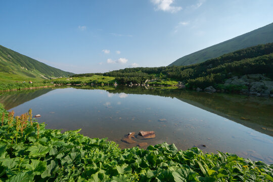 View of Bystre pleso lake reflecting the blue sky and surrounding green mountain slopes in the Low Tatras National Park Liptovsky Mikulas, Zilinsky kraj, Slovakia.