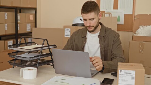 Man at packing desk stretches and rubs neck beside laptop and parcels in packing building; relief small business.