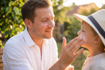 Fototapeta premium Caring father applying sunscreen to his young son face outdoors