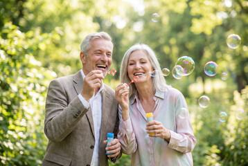 Fototapeta premium Happy senior couple blowing soap bubbles in a green park