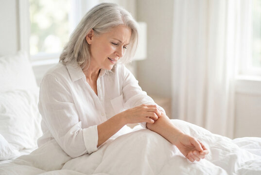 Mature woman scratching itchy arm while sitting in white bed