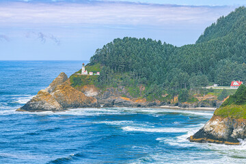 Heceta Head Lighthouse stands on a forested headland above the Pacific Ocean, with a coastal highway visible along the rugged Oregon shoreline. © ZL Visuals