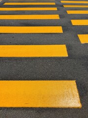 Fototapeta premium Top view of vibrant yellow pedestrian crosswalk patterns on dark asphalt street
