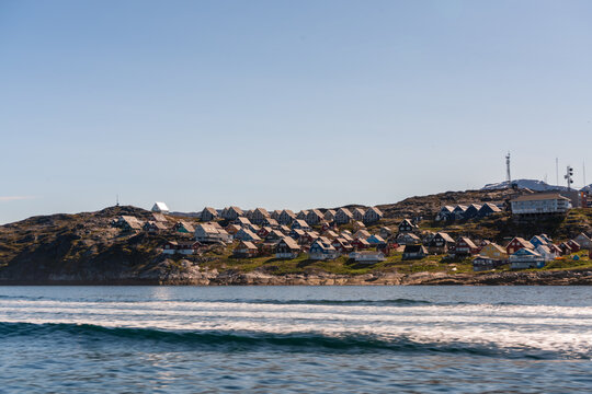 View of colorful houses scattered across a rocky hillside along the coastline under a clear blue sky in Nuuk, Sermersooq Municipality, Greenland.