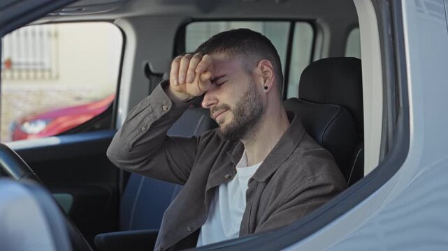 Man in car seated with hands raised and rubbing forehead beside steering wheel on street; frustration commute delay.