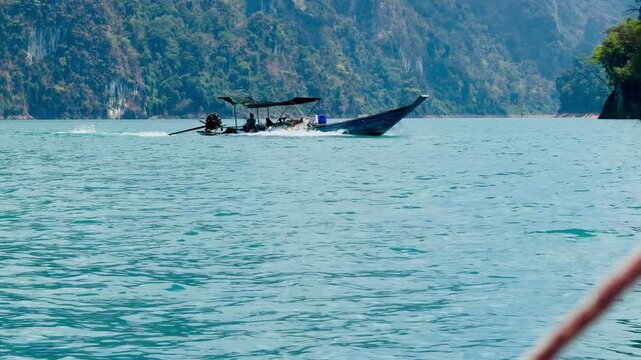 Tourists on a long-tail boat cruising past gigantic limestone cliffs at Cheow Lan Lake. An epic view of the Avatar-like mountain peaks and emerald waters in Khao Sok National Park, Thailand.