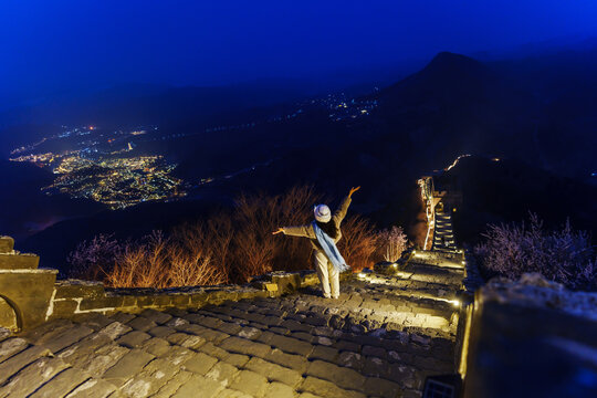 Young happy woman traveler enjoying and looking at night view of the Illuminated Great Wall of China