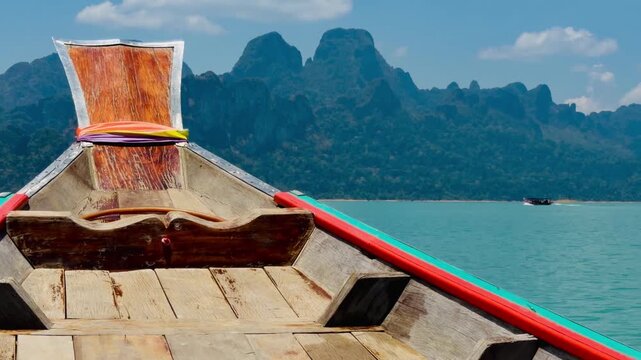 Vibrant prow of a traditional long-tail boat decorated with saffron ribbons on Cheow Lan Lake. An iconic symbol of Thai travel culture amidst the limestone mountains of Khao Sok, Thailand.