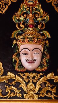 Close up of a divine Deva face with intricate golden carvings at Wat Maha That Wachiramongkol in Krabi, Thailand. Symbol of spiritual protection and Thai Buddhist craftsmanship on dark background. Art