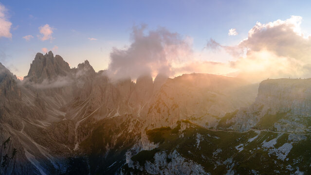 View of the jagged peaks of the Dolomites partially shrouded in soft clouds during a golden sunset in Trentino-South Tyrol, Italy.