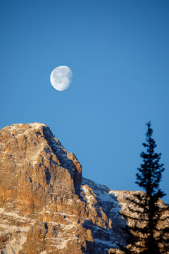 View of the rugged Dolomites mountain peaks with snow patches under a clear blue sky and a bright moon Trentino-South Tyrol, Italy.
