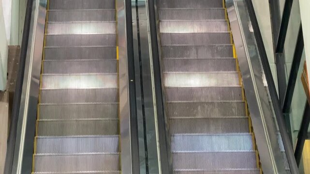 High-angle top view of two escalators moving in opposite directions in a public space like a mall or office.