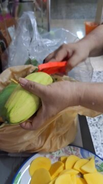 Vertical 4K close up of woman peeling a ripe mango with a knife.