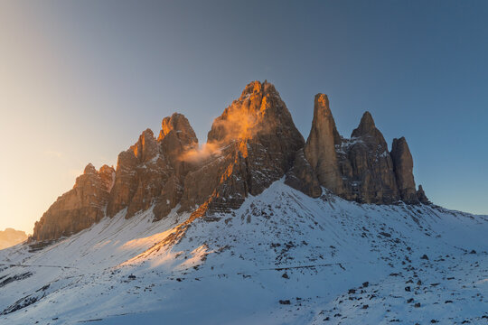 View of the snow-covered Tre Cime di Lavaredo peaks glowing under golden hour light in Trentino-South Tyrol, Italy.