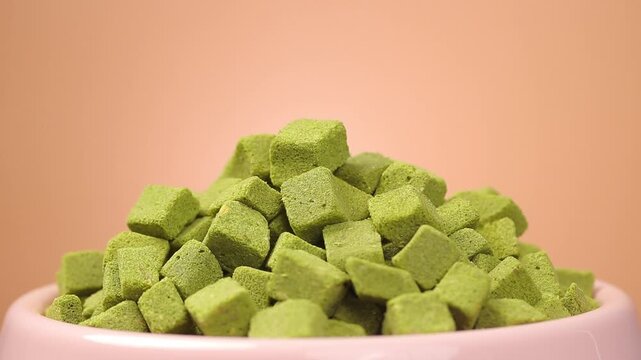 pile of freeze dried cat grass cube rotating slowly in a pet bowl on  a peach background. close-up view