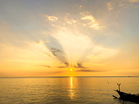 Stunning Golden Sunset over Calm Sea with Crepuscular Rays and Boat Silhouette