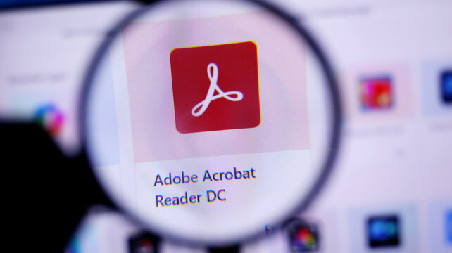 Closeup of adobe acrobat reader dc icon on a computer screen through a magnifying glass