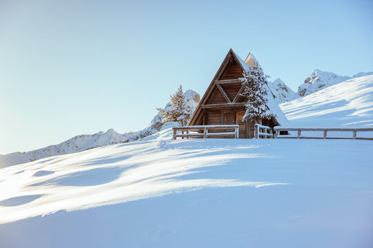 View of a traditional wooden A-frame cabin nestled in a deep snow-covered mountain landscape under a clear blue sky Trentino-South Tyrol, Italy.