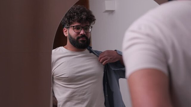 Young man with beard getting dressed in front of mirror