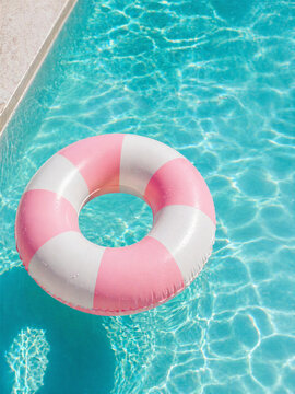 Pink and white inflatable pool floats on clear turquoise swimming pool water in summer sunlight