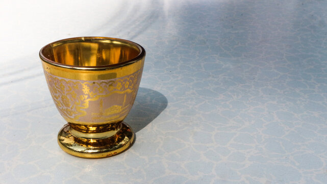 Arabic mini tea cup. Close-up of a small golden cup placed on a light textured surface. Minimalist composition highlighting the shiny metallic finish 