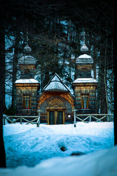 View of the historic Russian Chapel with its intricate wooden architecture and snow-covered roof surrounded by a dark pine forest in winter Slovenia.