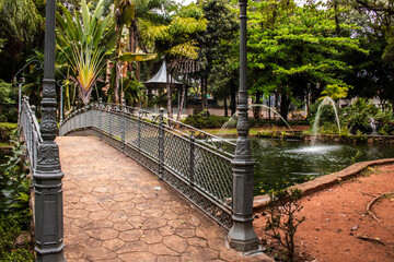 View of a classic metal bridge crossing a pond with fountains at a public garden in the city of Amparo, Sao Paulo state,