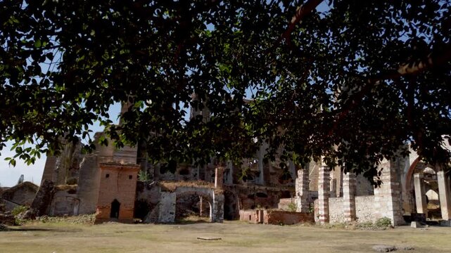 Abandoned hacienda ruins with broken walls and arches, open yard in front, large structure showing decay, historic architecture and quiet rural environment under clear sky