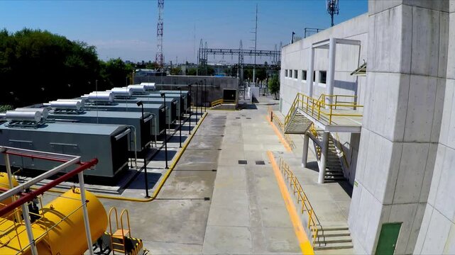Drone view of industrial facility with machinery units pipelines and storage tanks with concrete structures and organized layout under bright daylight