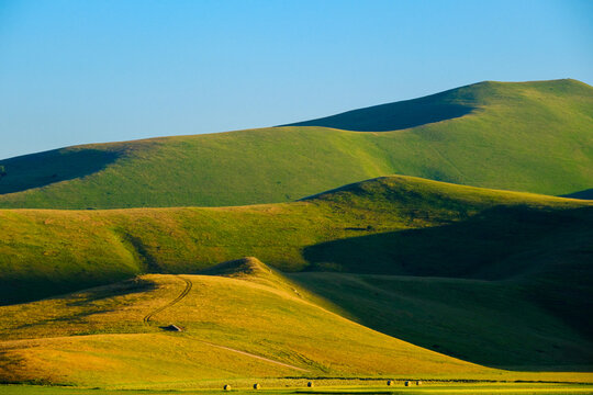 View of the rolling green hills with soft shadows and golden sunlight under a clear blue sky Castelluccio, Umbria, Italy.