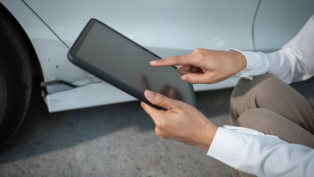 Hands of an auto inspector holding a tablet, documenting a dent and scratches on a white car door, close-up at a repair shop, vehicle damage assessment and insurance claim concept.